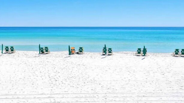 A beach with rows of green lounge chairs facing the ocean.