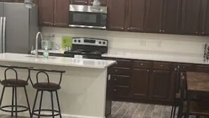 A modern kitchen with dark wooden cabinets, a central island with stools, and a stainless steel refrigerator.
