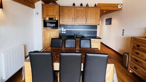 Uma cozinha compacta com armários de madeira, uma ilha central e uma mesa de jantar com cadeiras.