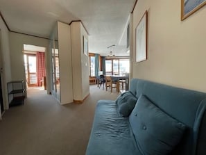 Ein Wohnzimmer mit einem blauen Sofa, ein Essbereich mit Tisch und Stühlen sowie eine Küche im Hintergrund.