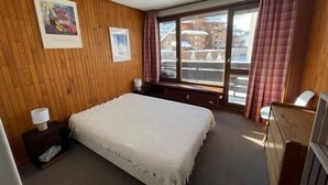 A hotel room with a bed, a window with curtains, a wooden wall, and a painting. - 300m from ski slopes, 3rd floor, balcony, tv, ski locker, 52m², Tignes (Tignes)