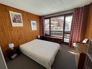 Ein Hotelzimmer mit Bett, Fenster mit Vorhängen, einer Holzwand und einem Gemälde.