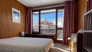 A bedroom with a large bed, wooden walls, a window with curtains, and a view of mountains. - 300m from ski slopes, 3rd floor, balcony, tv, ski locker, 52m², Tignes (Tignes)