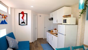 Ein kompakter Wohnraum mit Küchenzeile, einer Couch mit Kissen, einem Esstisch mit Stühlen und einem Wandbild.