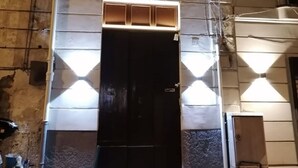 Ein Gebäude mit einer dunklen Eingangstür, einem kleinen Fenster mit Metallgitter und einer gefliesten Fassade.