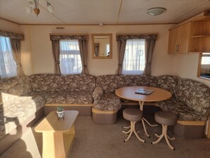 A cozy RV interior with a sectional sofa, a small table, and a round table with stools. - Ingoldmells Coral Beach on Entrance (Skegness)