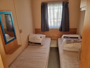 A compact hotel room with two beds, a small window with curtains, a mirror, and a bedside table. - Ingoldmells Coral Beach on Entrance (Skegness)