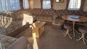 A cozy RV interior with a sectional sofa, a small wooden table, and a round table with chairs. - Ingoldmells Coral Beach on Entrance (Skegness)