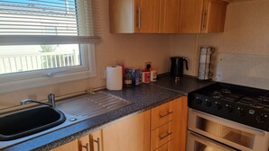 A kitchen with wooden cabinets, a stainless steel stove, a sink, and a window with blinds. - Ingoldmells Coral Beach on Entrance (Skegness)