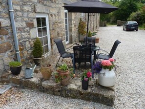 A stone building with a gravel patio, outdoor seating with chairs and a table, potted plants, and a parked car in the background. - La Longere a tranquil, rural stone cottage, cosy and comfortable. All inclusive (Lonlay-l'Abbaye)