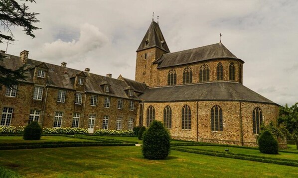 A large stone building with a prominent tower and multiple windows, surrounded by well-maintained lawns and hedges. - La Longere a tranquil, rural stone cottage, cosy and comfortable. All inclusive (Lonlay-l'Abbaye)