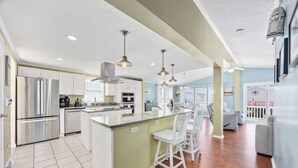 A modern kitchen with stainless steel appliances, a central island with bar stools, and a dining area with a view.