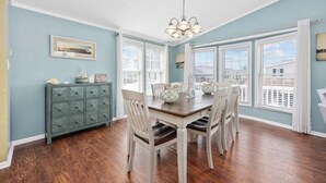 A dining area with a wooden table and chairs, a chandelier, and a view through large windows.