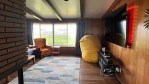 Un salon moderne avec une grande fenêtre, un téléviseur fixé au mur, un fauteuil en forme de poire jaune et une petite table.