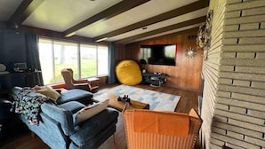 Un salon moderne avec un canapé, des fauteuils, un téléviseur et une grande fenêtre.