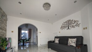 A spacious living area with a dark sofa, a dining table, and a large window. - 3 Bed House - Sleeps 7 - Garden - Parking - Wifi (Birmingham)