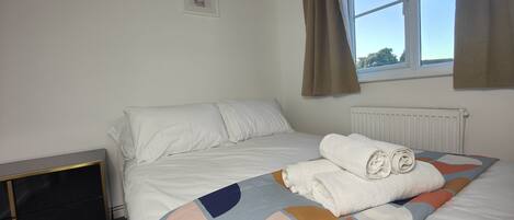 A bedroom with a bed, a radiator, a window with curtains, and a small framed picture on the wall.