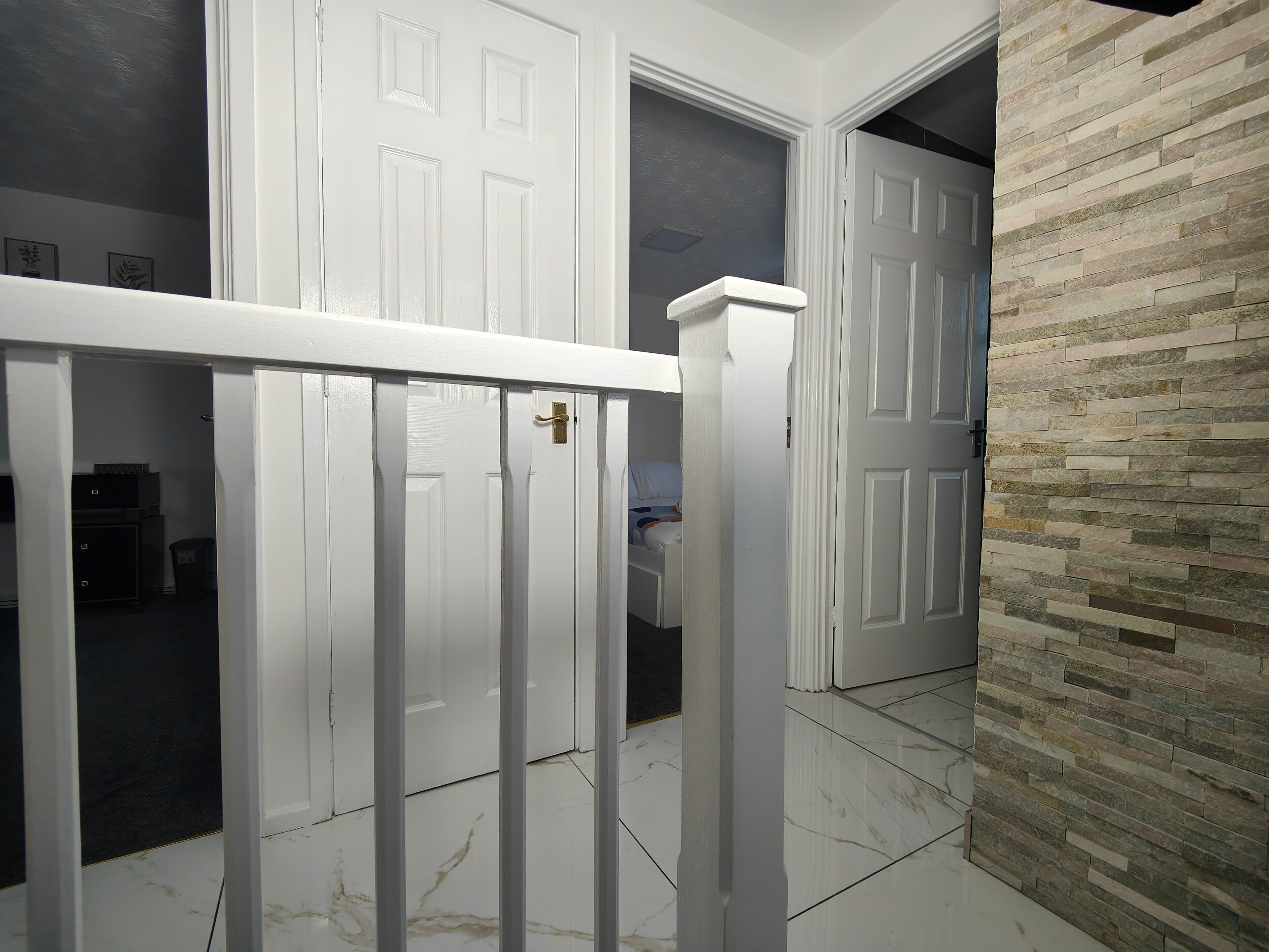 A hallway with white doors, a white railing, and a stone wall.