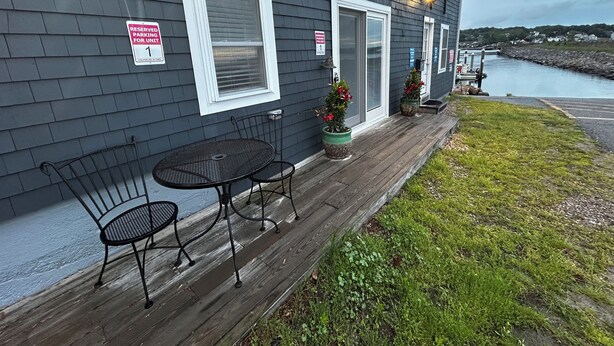 A dark grey building with a wooden deck, a metal table and two chairs, and two potted plants. - Marina on the Sakonett (Portsmouth)