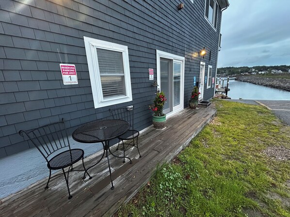 A dark grey building with a wooden deck, a metal table and two chairs, and two potted plants. - Marina on the Sakonett (Portsmouth)