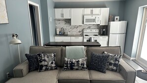 A modern living room with a sectional sofa, a wooden coffee table, and a kitchen area with white cabinets, a microwave, and a refrigerator. - Marina on the Sakonett (Portsmouth)