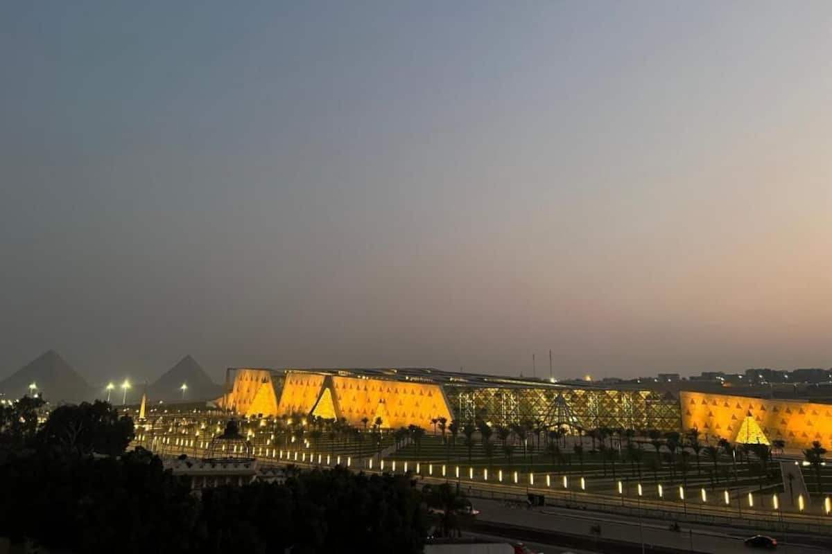 A large, illuminated building with a distinctive triangular facade, surrounded by a well-lit plaza and a road in the foreground.