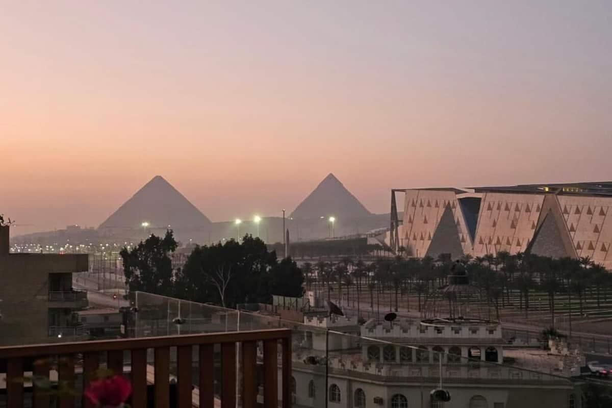 A view of the pyramids at sunset with modern buildings in the foreground.