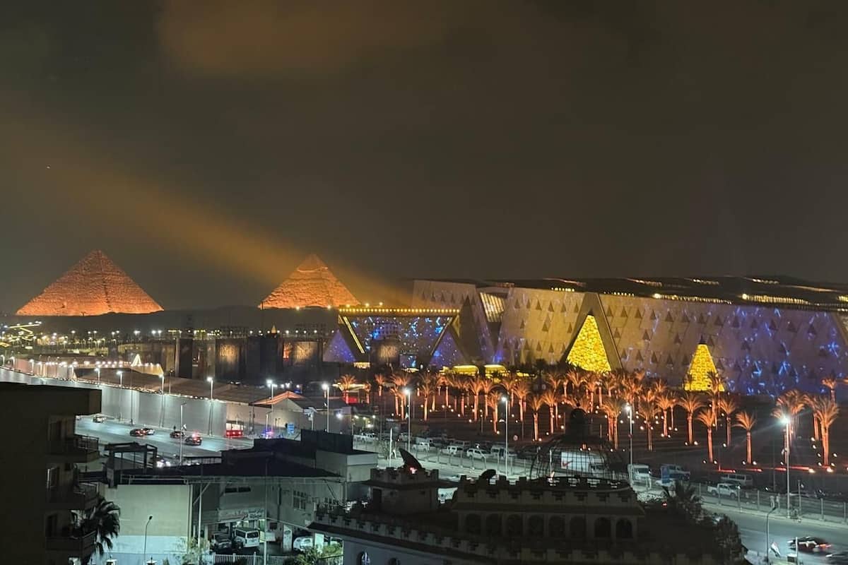 A nighttime view of a cityscape with illuminated pyramids and a large, modern building with geometric patterns.