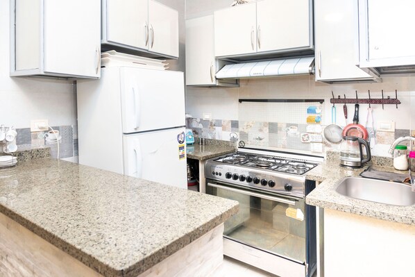 A kitchen with granite countertops, a gas stove, a refrigerator, and a sink. - Arkan Egyptian Museum Hotel (Giza)