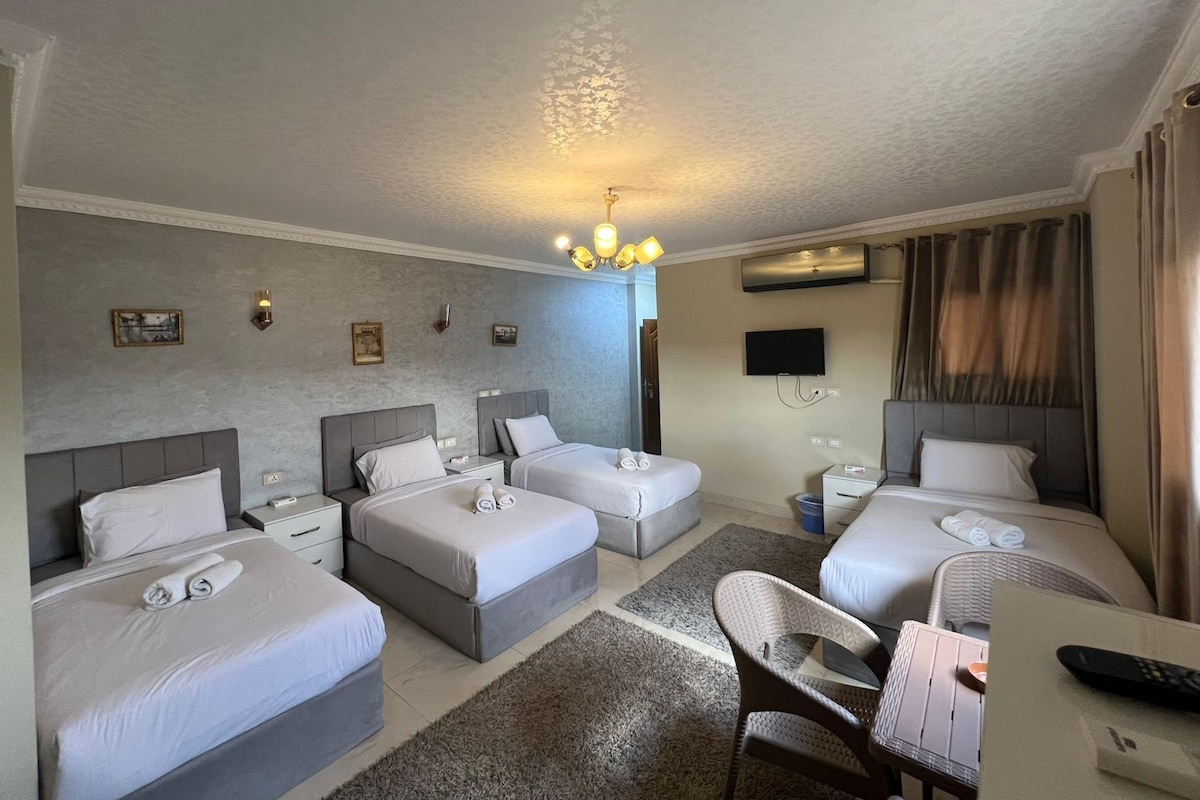 A hotel room with two single beds, a double bed, a TV, a flat-screen TV, a desk with a chair, and a remote control on the desk.