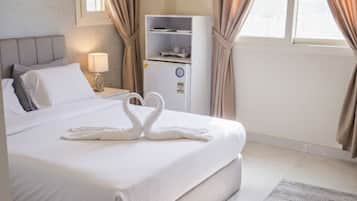A hotel room with a large bed, a minibar, a ceiling light fixture, and a window with curtains.