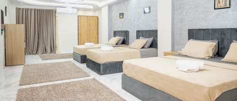 A modern hotel room with three beds, a wooden wardrobe, and a large window with curtains.