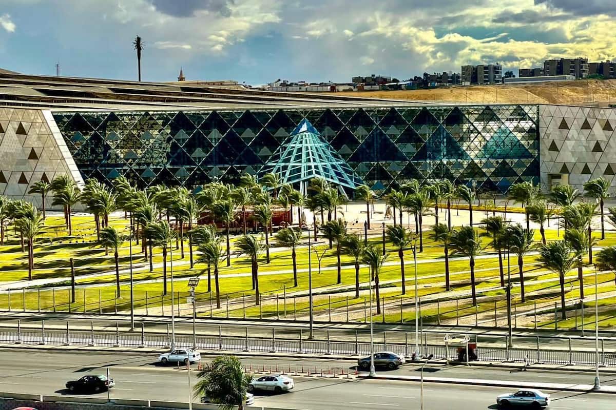 A modern building with a distinctive geometric glass facade, surrounded by a well-maintained lawn with palm trees.