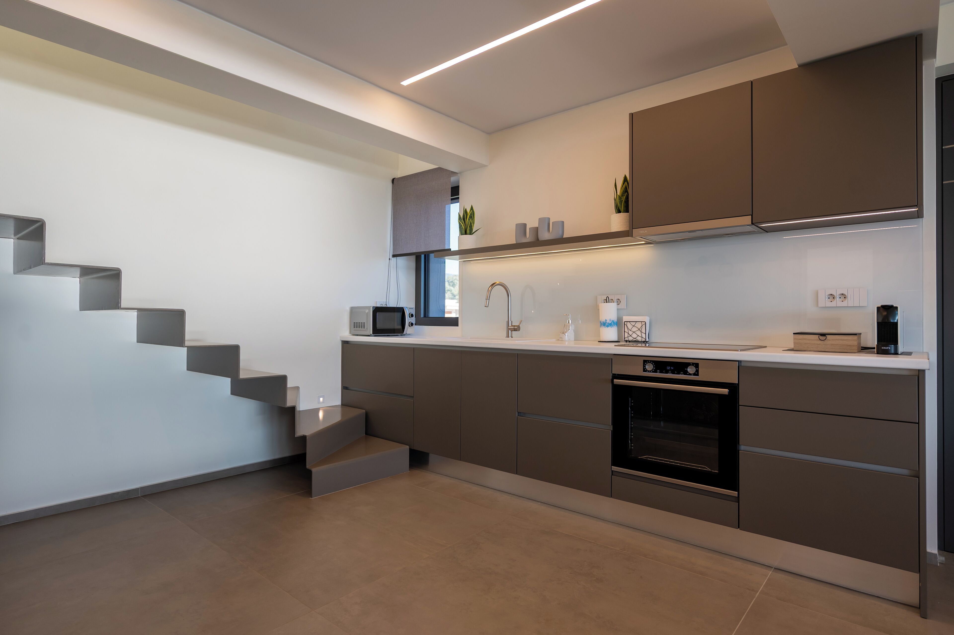 A modern kitchen with built-in appliances, a microwave, and a dishwasher. There is a staircase leading to another level.