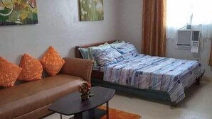 A room with a sofa, a bed with a striped bedspread, a small table with a vase, and a chair. - Saekyung Village One-Phase 2 (Lapu-Lapu City)