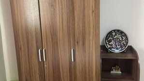 A wooden wardrobe with two doors and three drawers, accompanied by a small shelf with decorative items. - Saekyung Village One-Phase 2 (Lapu-Lapu City)