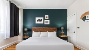 Une chambre à coucher avec un grand lit, des murs d’un vert turquoise foncé et une tête de lit en bois. On y trouve deux tables de chevet avec des lampes et des tableaux encadrés accrochés au mur.