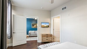 Un dormitorio con una cama, un aparador de madera, una puerta blanca y una pared azul con un cuadro.