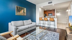 Un salón con un sofá gris, una mesa de centro de vidrio y una pared azul con un cuadro de leopardo.