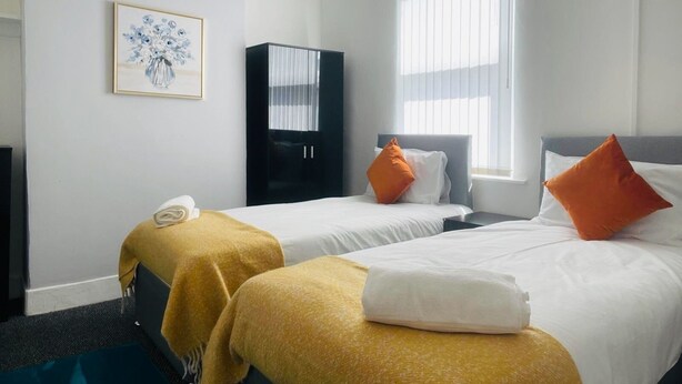 A hotel room with two beds, a wardrobe, a painting, and a window with blinds. - Remarkable 4-bed House in Bootle, Liverpool (Bootle)