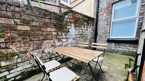 A rustic outdoor seating area with a wooden table and chairs, set against a brick wall with a window. - Remarkable 4-bed House in Bootle, Liverpool (Bootle)