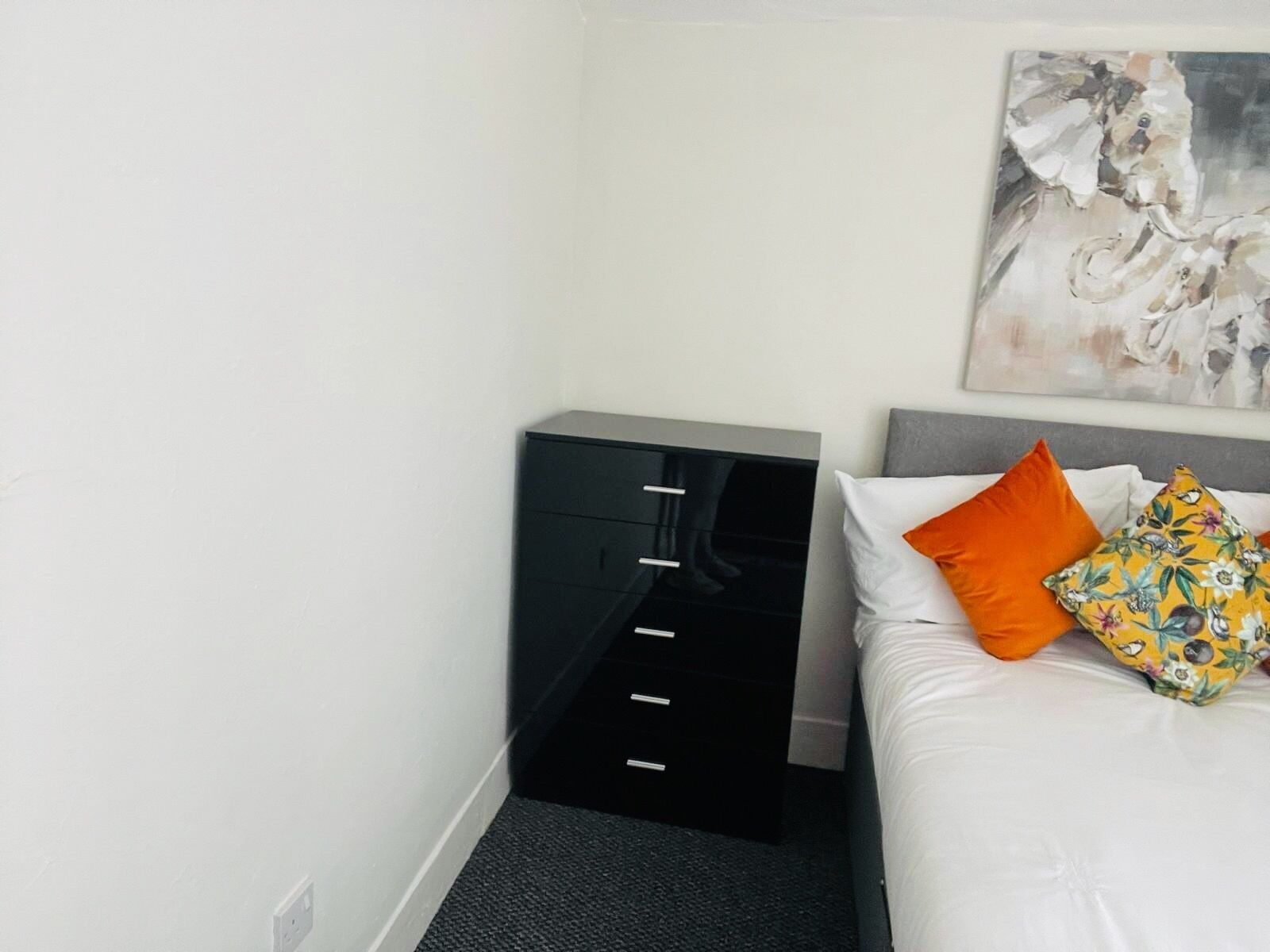 Una habitación de hotel con una cama, un archivador negro y un cuadro en la pared.