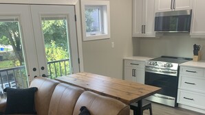 A modern kitchen with white cabinets, a stainless steel stove, and a wooden dining table. - Gem on Prospect (Kingsville)