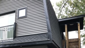 A two-story house with a black exterior, a garage, and a wooden staircase leading to a deck. - Gem on Prospect (Kingsville)