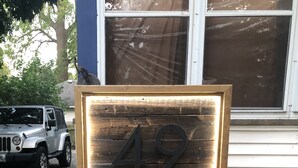 A wooden house number sign with the number 49, placed in front of a house with a gravel driveway and a parked car. - Gem on Prospect (Kingsville)