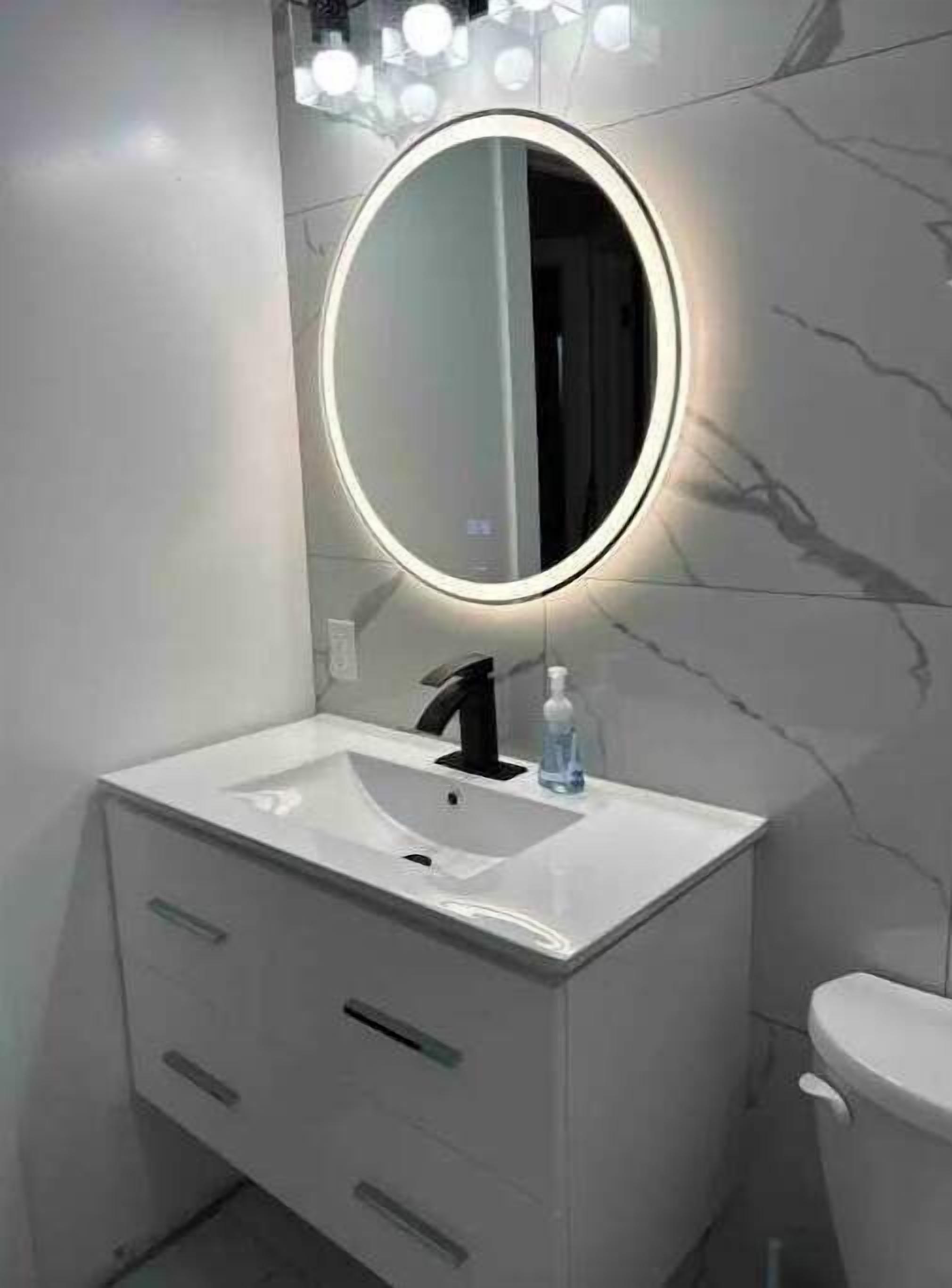 A bathroom with a white vanity, a round mirror with lights, a black faucet, and a white toilet.
