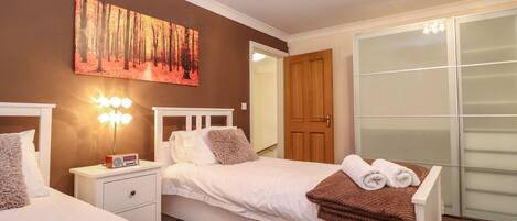 A hotel room with two beds, a nightstand with a lamp, a painting on the wall, and a wardrobe.