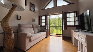 Un salon spacieux doté d’un plancher en bois, d’un canapé beige, d’un téléviseur et d’une grande fenêtre donnant sur l’extérieur.