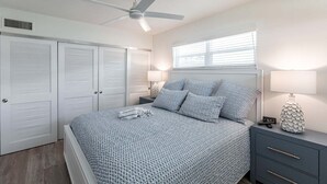 A bedroom with a bed, a ceiling fan, a window, and a nightstand with a lamp. - Villa 05 - Premium - Aloha Kai Vacation Villas (Siesta Key)