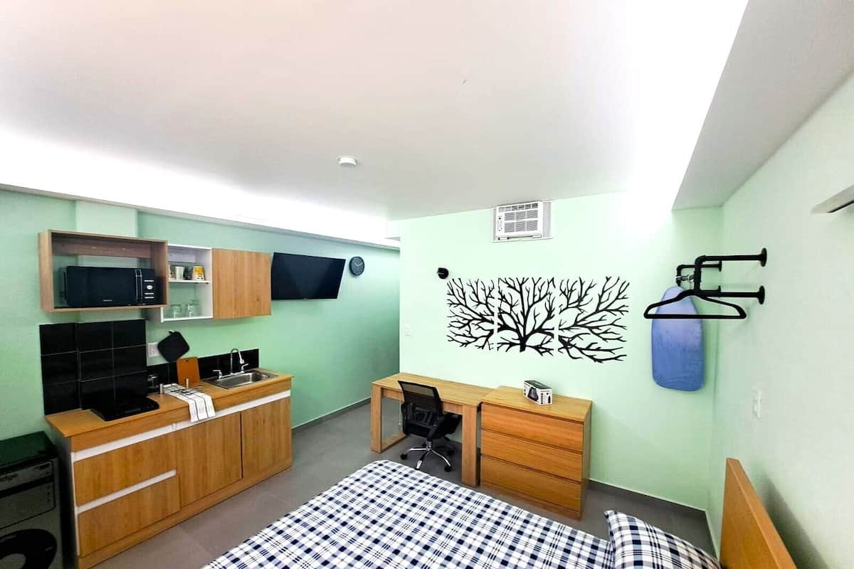 A compact bedroom with a bed, a desk, a chair, a microwave, a TV, and a wardrobe.